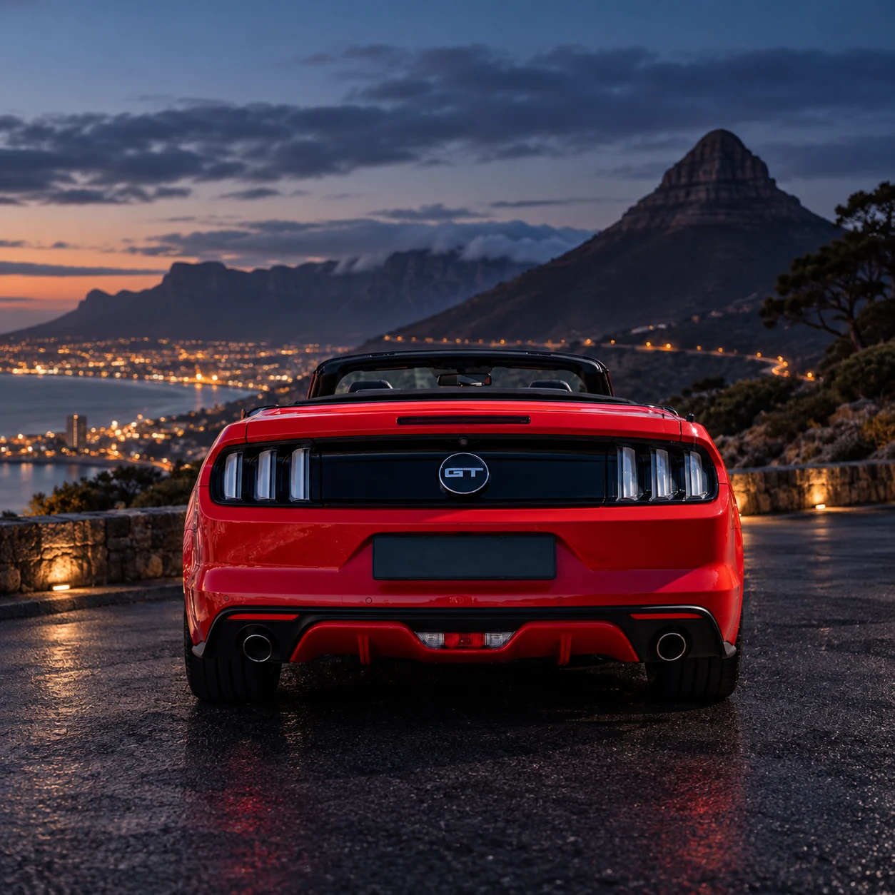 Red Ford Mustang GT Convertible with the top down, rear view with a mountain and city lights behind